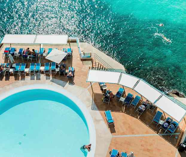 Lentotuoleja ja uima-allas meren äärellä, kuvattu ylhäältä. (Tekoälyn luoma teksti)