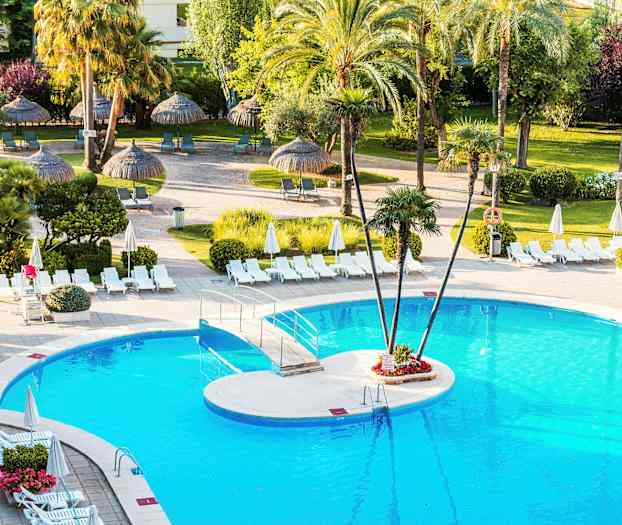 Uima-allas, jota ympäröivät aurinkotuolit ja aurinkovarjot, taustalla palmuja ja vehreää kasvillisuutta. (Tekoälyn luoma teksti)