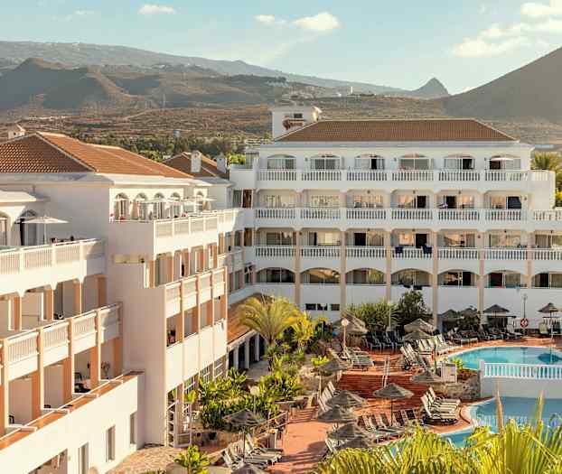 Hotellirakennus uima-allasalueella ja aurinkotuoleilla, vuoristomaiseman ympäröimänä. (Tekoälyn luoma teksti)