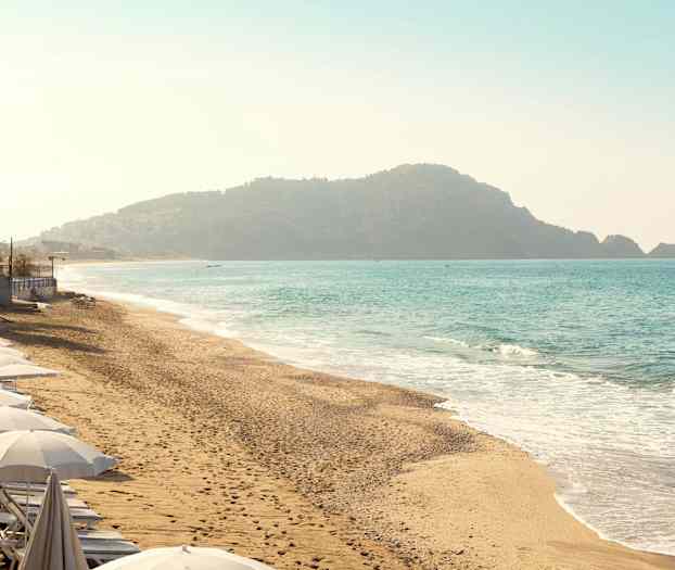 Ranta varjoineen rannikkoviivaa pitkin ja taustalla vuoria meren äärellä. (Tekoälyn luoma teksti)