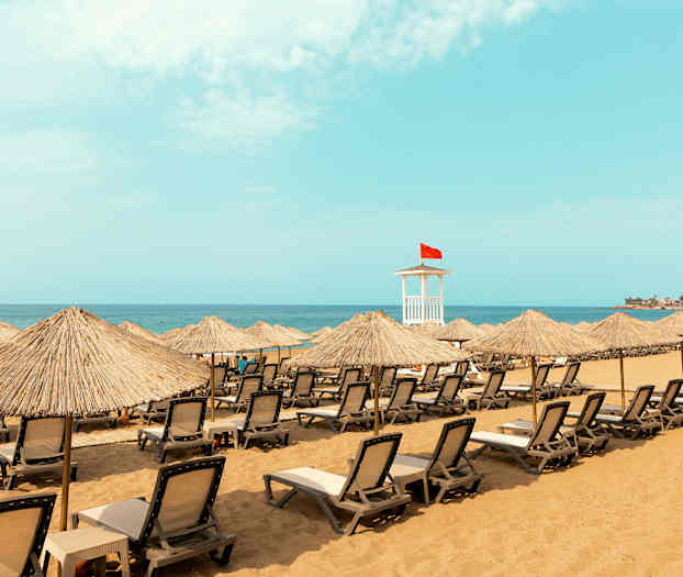 Ranta, jossa on aurinkotuoleja ja varjostimia sekä pelastajan torni, jossa on punainen lippu. (Tekoälyn luoma teksti)