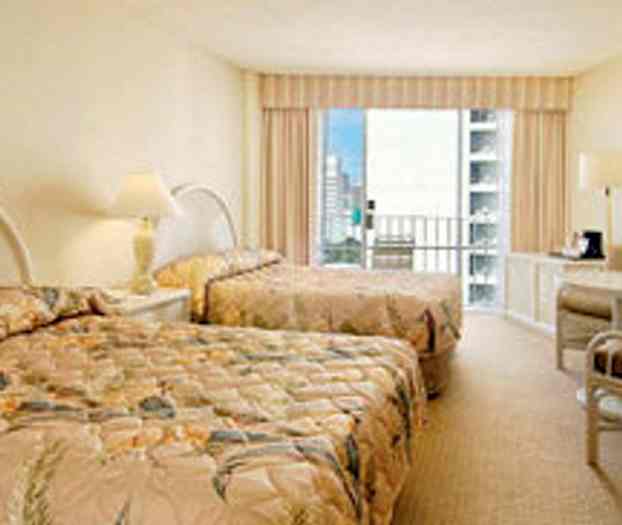 Hotellihuone, jossa kaksi kukkakuvioisilla päiväpeitteillä varustettua sänkyä, pieni huonekalu kahvinkeittimellä ja parveke, jolta on näkymä kaupunkiin. (Tekoälyn luoma teksti)