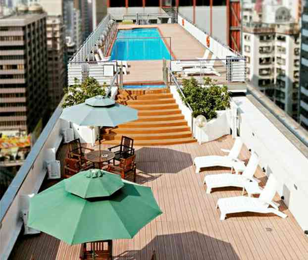 Kattoterassi, jossa on aurinkotuoleja, ruokapöytiä ja aurinkovarjoja sekä uima-allas taustalla. (Tekoälyn luoma teksti)