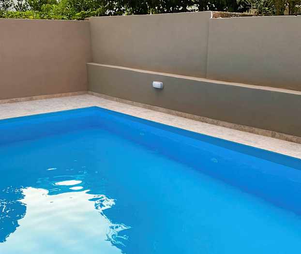 Ulkoallas, jossa on kirkas sininen vesi, ympäröitynä beigellä muurilla ja vehreydellä taustalla. (Tekoälyn luoma teksti)