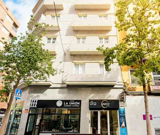 Kerrostalo, jossa parvekkeita, liiketiloja pohjakerroksessa ja jonkin verran vehreyttä ympärillä. (Tekoälyn luoma teksti)