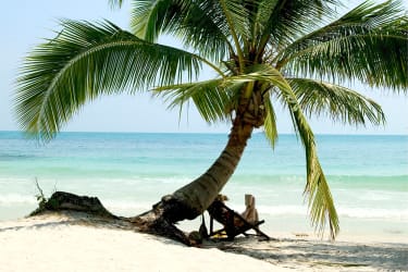 Koh Sametin vaaleahiekkaista rantaa, palmun varjoon asetetti aurinkotuli, jossa nainen lukee kirjaa.