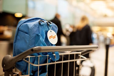 Matkalaukkukärryssä oleva sininen reppu, jossa on logolla varustettu nimilappu.