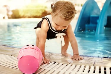 Pieni tyttö leikkii ämpärin kanssa uima-altaan reunalla