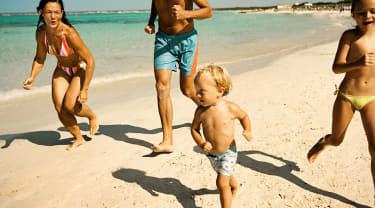 Lapsiperhe juoksee rannalla pakettimatkalla