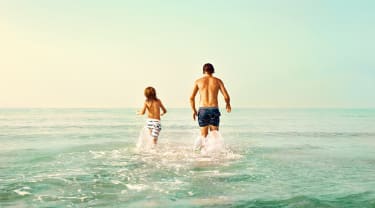 Isä ja poika juoksevat mereen - kesämatkat