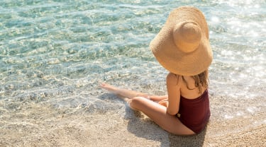 Nainen istuu hiekkarannalla veden äärellä