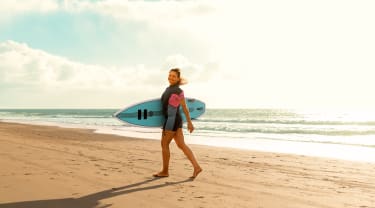 Nainen surffilauta kainalossa rannalla