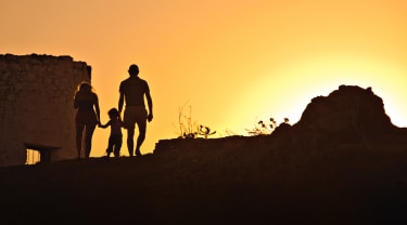 Isä, äiti ja pieni lapsi auringon laskiessa taustalla