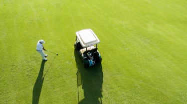 Golfauto ja pelaaja väylällä ylhäältä kuvattuna