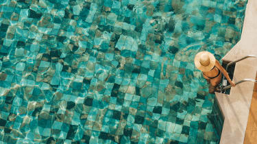 Nainen laskautumassa tikkaita uima-altaaseen aurinkohattu päässä