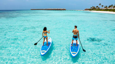 Pariskunta SUP-laudoilla turkoosinsinisellä merellä Malediiveilla