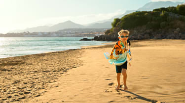 Pieni poika juoksee uimaleluja kantaen hiekkarannalla