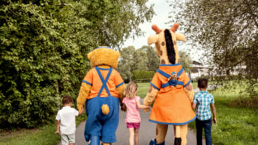 Lollo & Bernie kävelevät puistossa käsi kädessä kolmen lapsen kanssa. Kuva on otettu takaapäin.