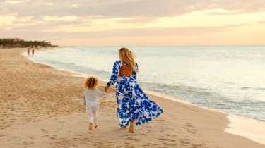 Nainan ja lapsi kävelemässä rannalla auringon laskiessa