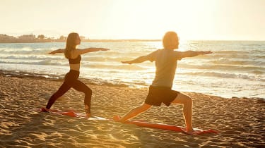 Nainen ja mies joogaamassa rannalla auringon noustessa