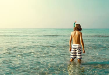 Poika seisoo vedessä snorkkeli kasvoilla ja katsoo veteen
