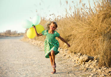 Lapsi juoksee rantahiekalla ilmapalloja kädessään pidellen