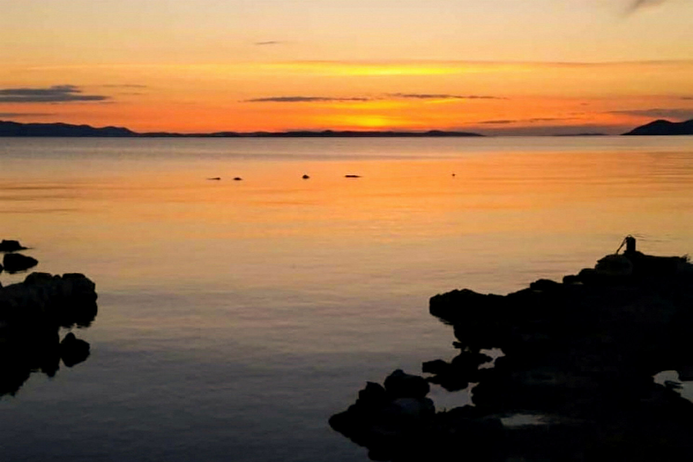 Auringonlasku rauhallisen meren yllä, kallion siluetteja etualalla. (Tekoälyn luoma teksti)