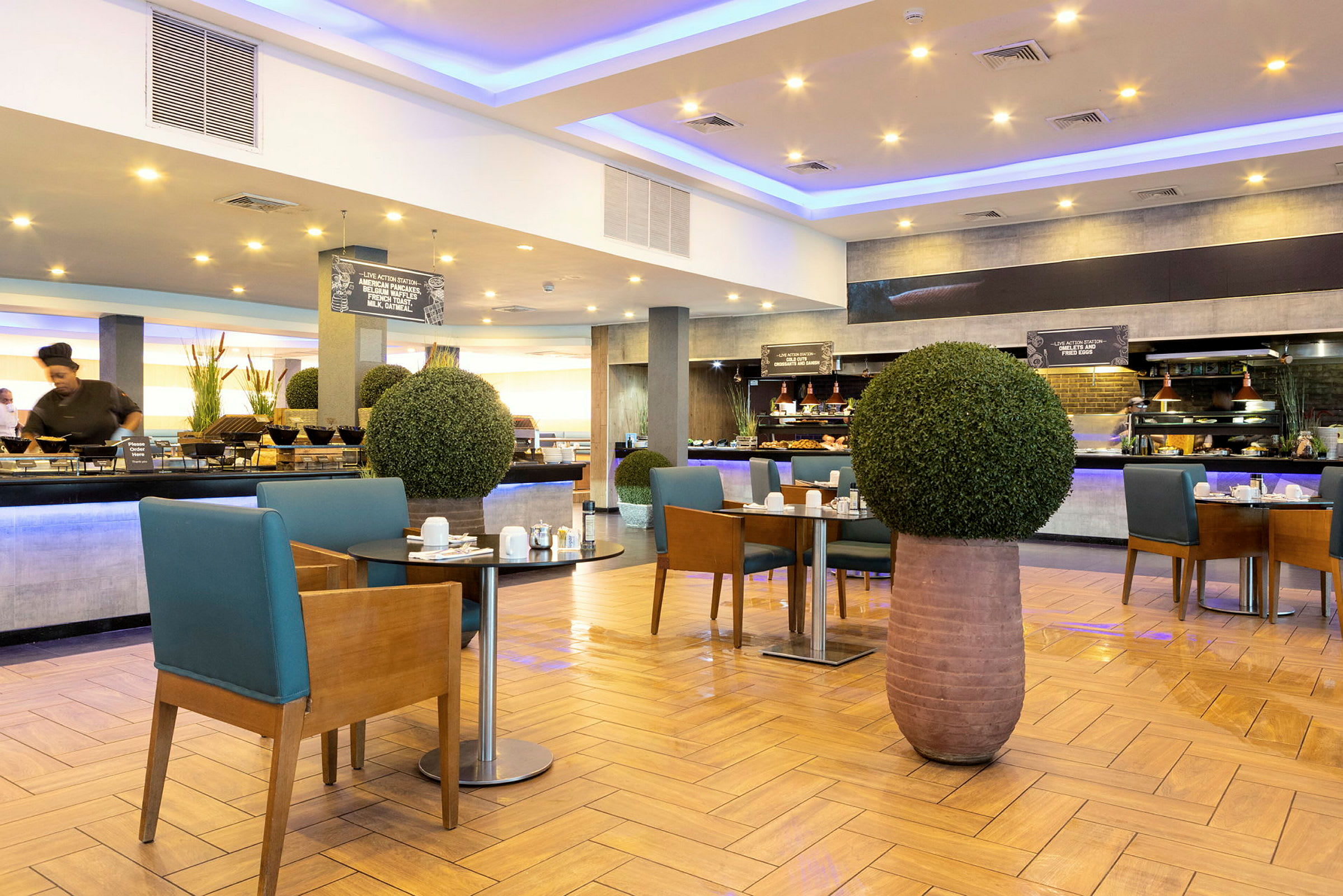 Moderni hotelliravintola, jossa on aamiaispöytä ja vihreillä kasveilla koristeltuja pöytiä. (Tekoälyn luoma teksti)