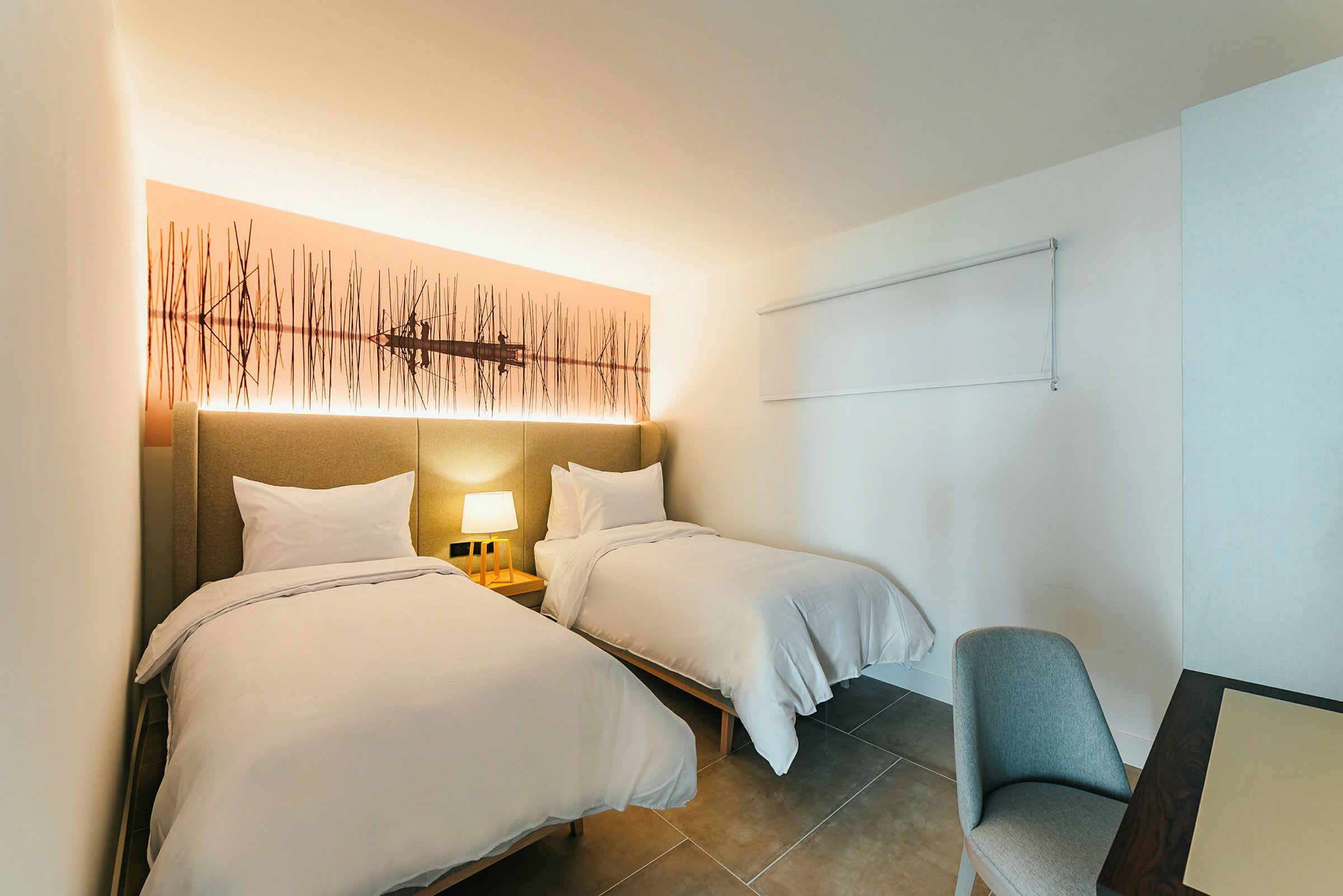 Hotellihuone, jossa kaksi yhden hengen sänkyä ja yölamppu. (Tekoälyn luoma teksti)