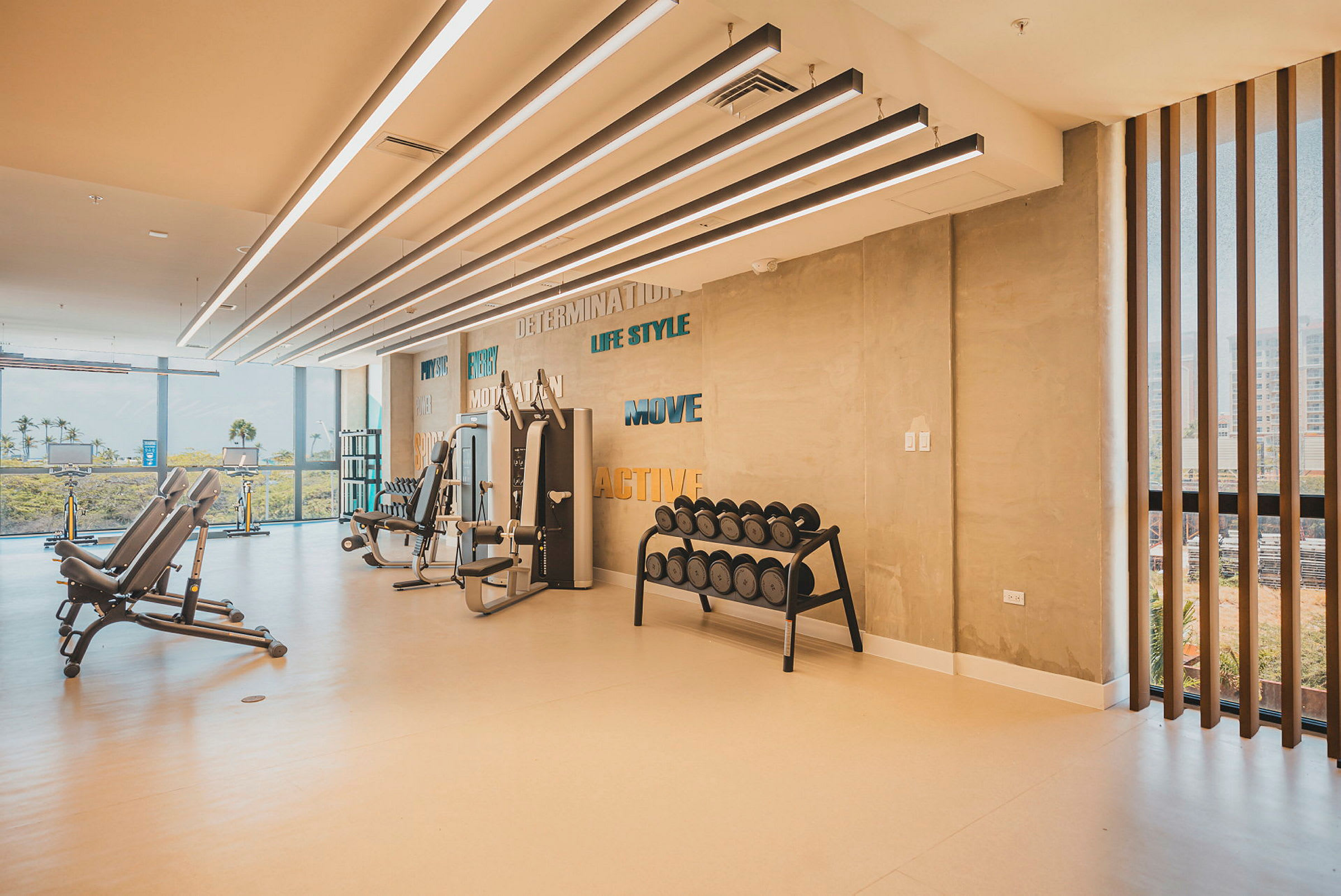 Moderni kuntosali, jossa harjoittelulaitteita ja käsipainoja, sekä suuret ikkunat, jotka päästävät valoa sisään. (Tekoälyn luoma teksti)