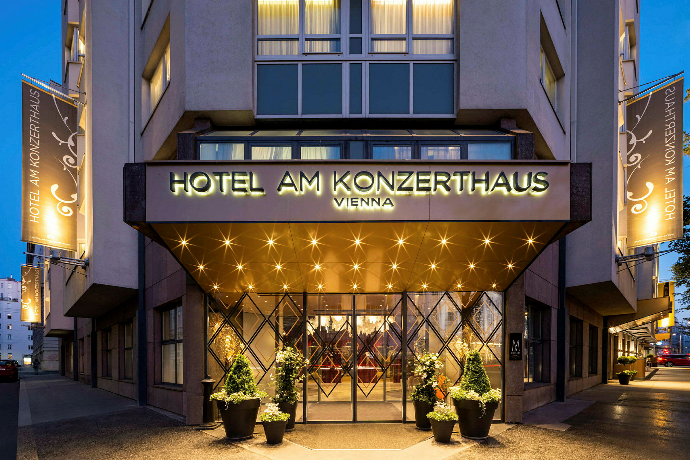 Hotellin sisäänkäynti, jossa on kyltti "Hotel am Konzerthaus Vienna". Valot ja koristeet näkyvät sisäänkäynnin ympärillä ja julkisivussa. (Tekoälyn luoma teksti)