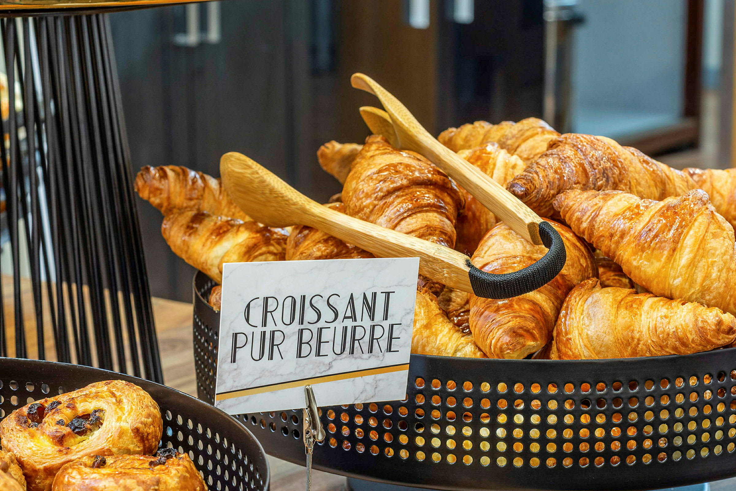 Kori täynnä vastapaistettuja croissanteja, joissa lukee kyltti 'Croissant Pur Beurre'. (Tekoälyn luoma teksti)