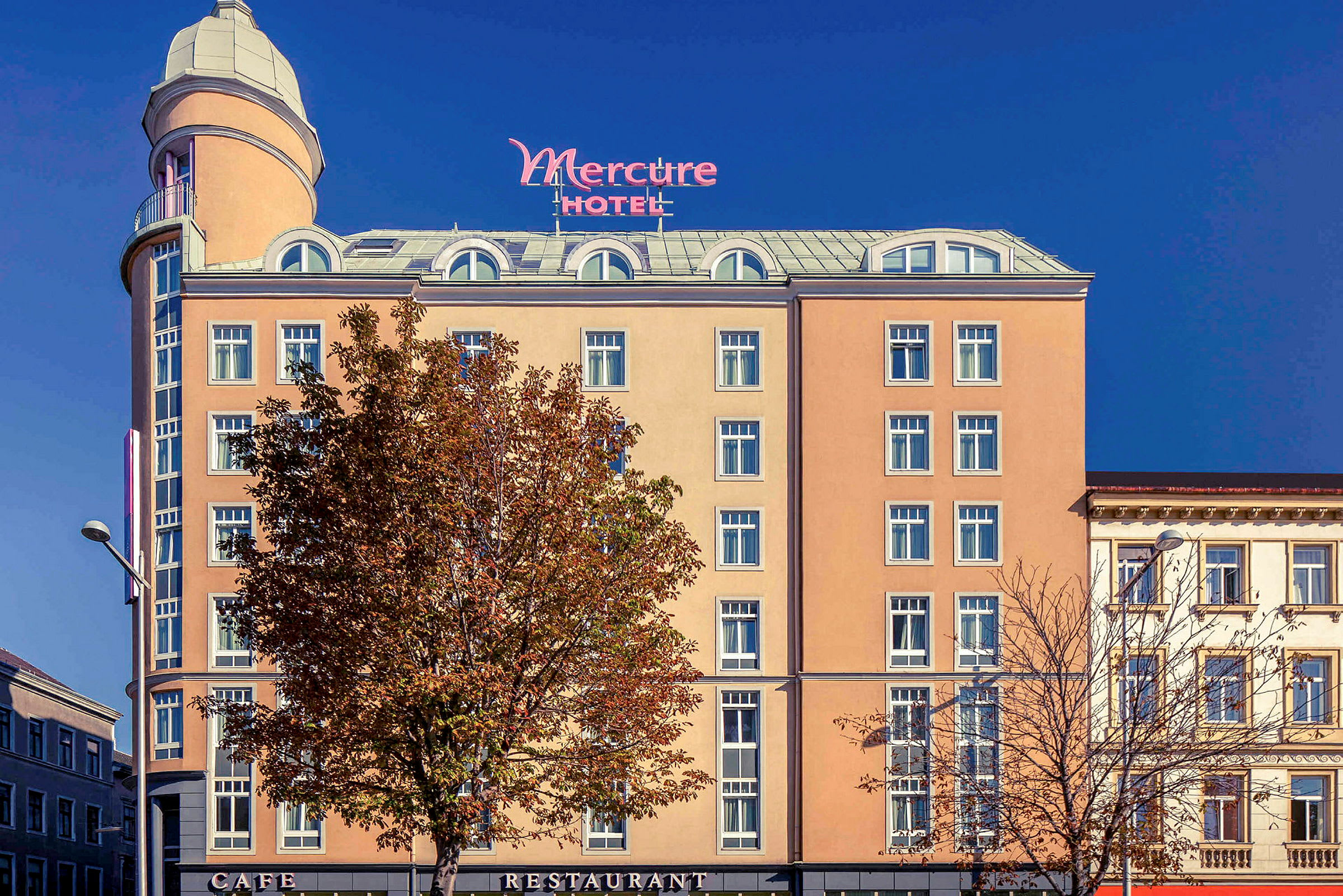 Hotellin Mercure ulkopuoli, jossa beige julkisivu, lukuisia ikkunoita ja korkea torni ylhäällä. (Tekoälyn luoma teksti)