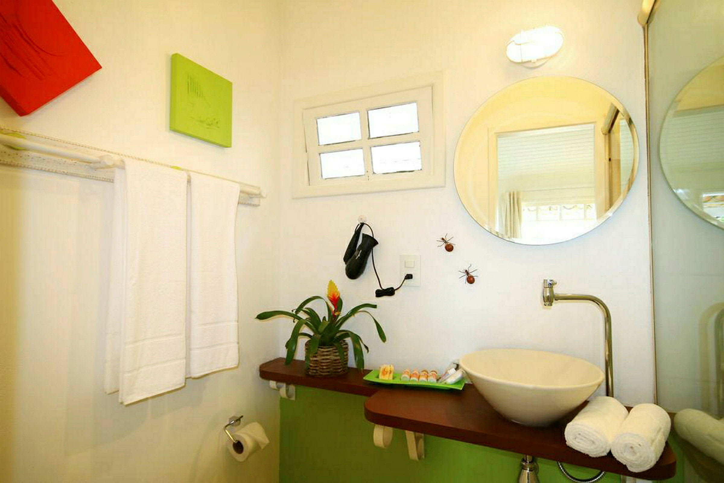 Kylpyhuone, jossa on pesuallas ja peili, koristeltu kasveilla ja koristeilla. Pyyhkeet ja wc-paperi näkyvissä. (Tekoälyn luoma teksti)