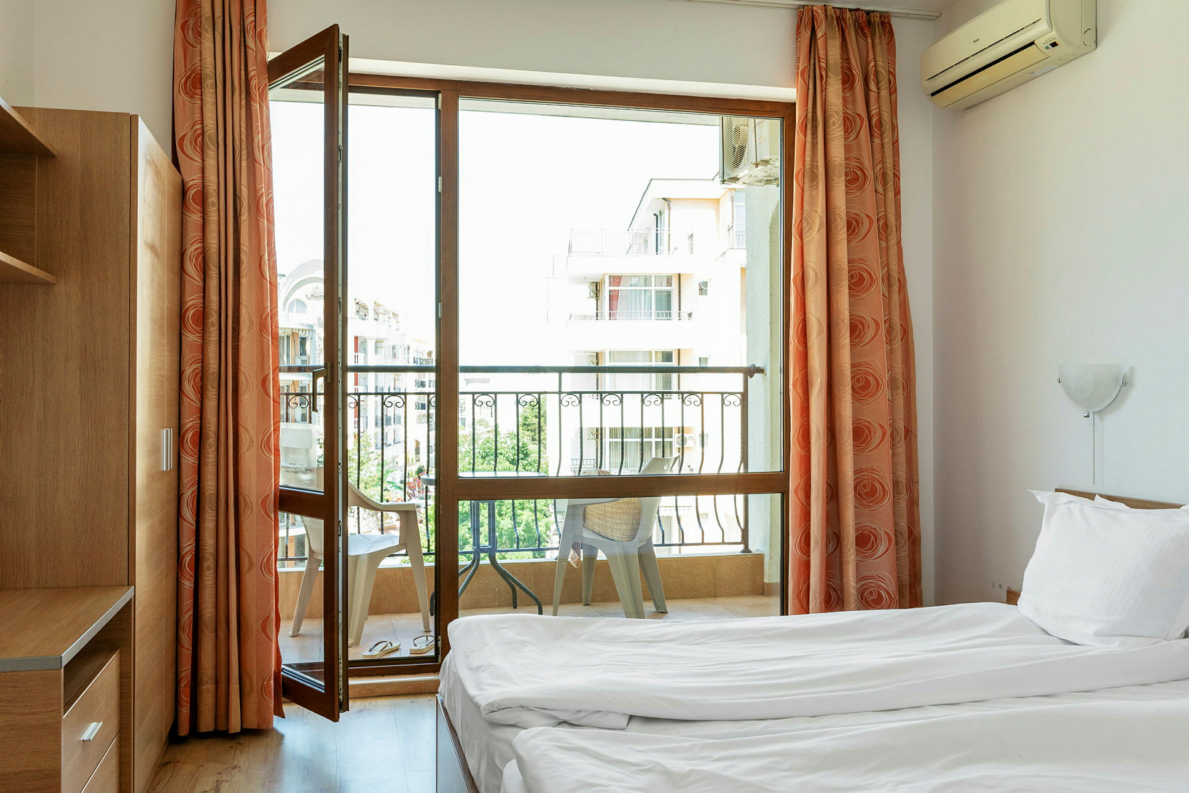 Hotellihuone, jossa on kaksi yhden hengen vuodetta ja ikkuna, joka johtaa parvekkeelle, jossa on tuoleja. (Tekoälyn luoma teksti)