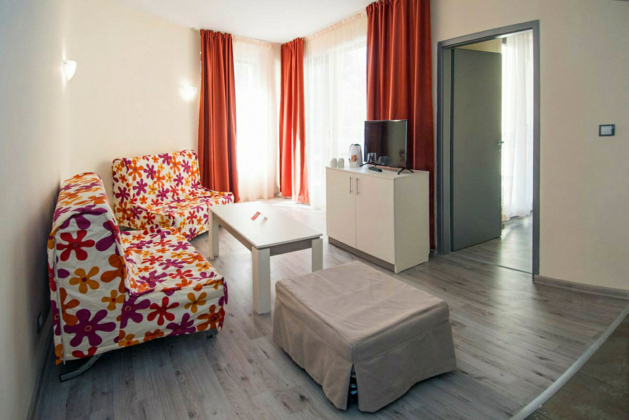 Olohuone värikkäillä sohvilla, sohvapöydällä ja televisiolla valkoisella huonekalulla. (Tekoälyn luoma teksti)