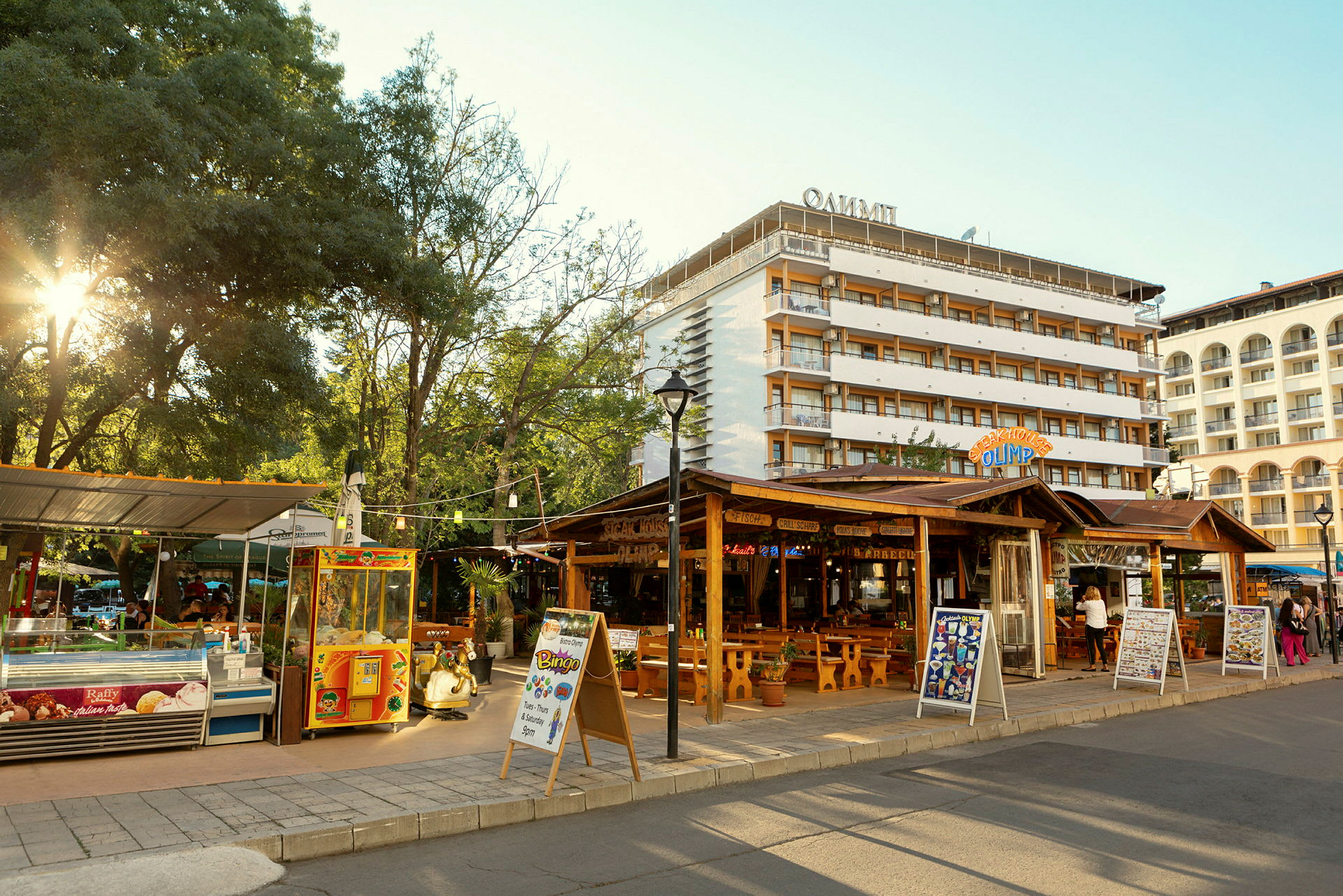 Katu, jossa on ravintoloita ja kauppoja, ja taustalla hotellirakennuksia. (Tekoälyn luoma teksti)