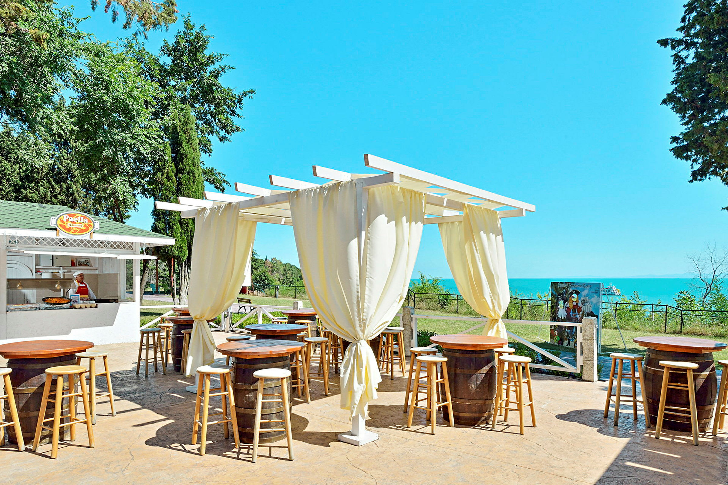 Ulkona sijaitseva ravintola, jossa on pergola, puisia pöytiä ja tuoleja sekä taustalla ruokatarjoilu. (Tekoälyn luoma teksti)