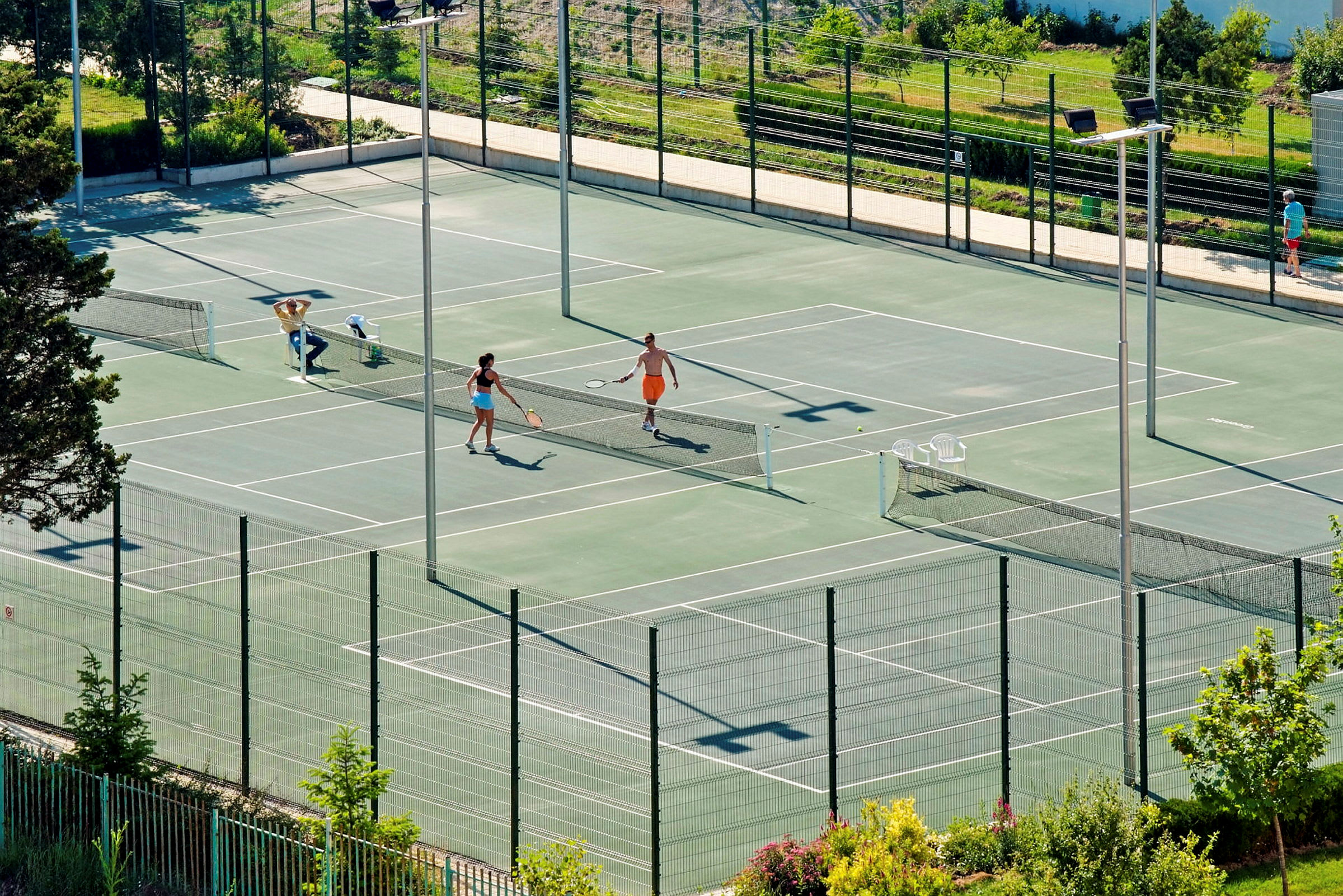 Kaksi henkilöä pelaa tennistä ulkokentällä vehreyden keskellä. (Tekoälyn luoma teksti)