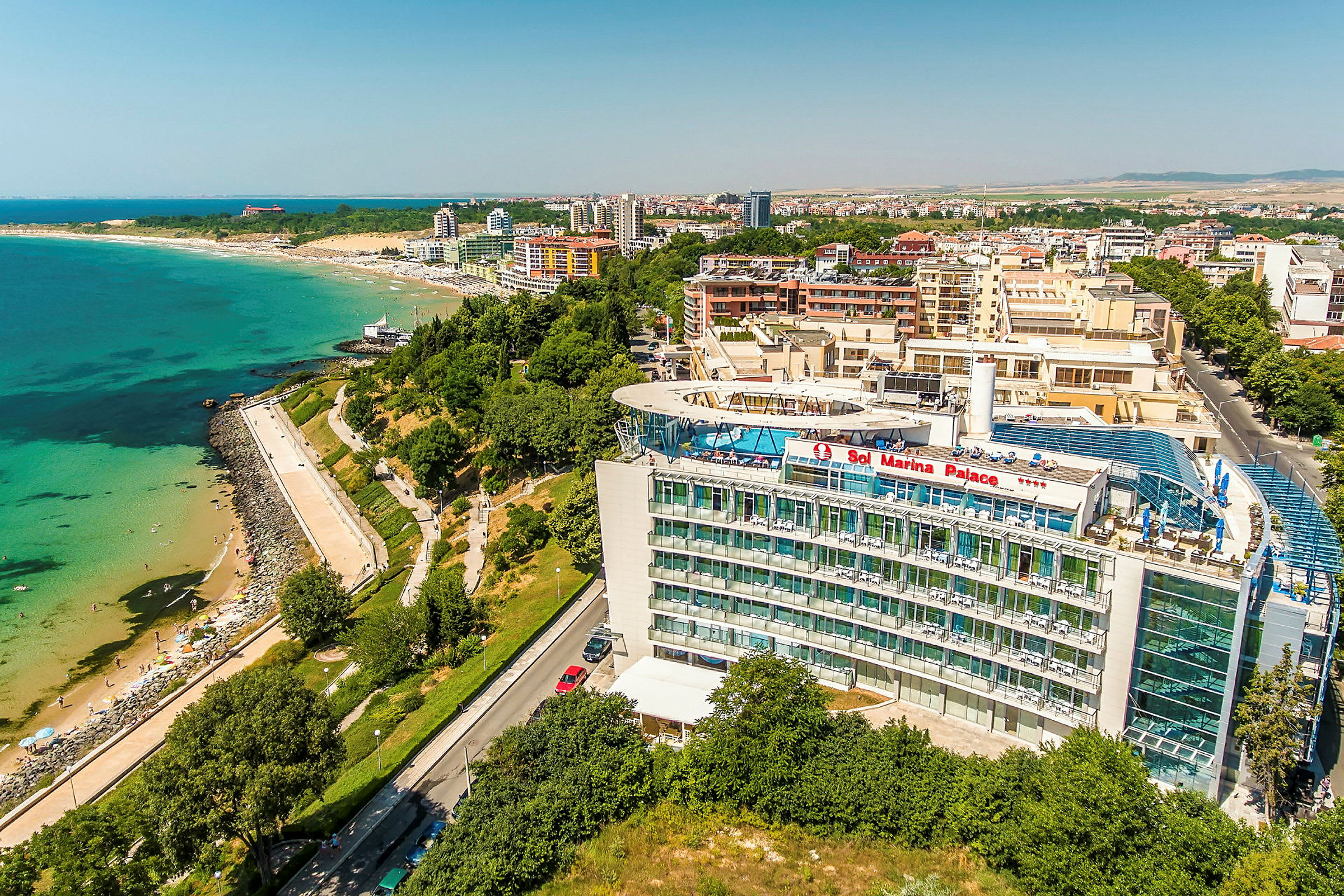 Ilmakuva hotellista, jossa lukee "Sol Marina Palace", sijaitsee lähellä rantaa ja rannikkoaluetta, jossa on kasvillisuutta ja rakennuksia taustalla. (Tekoälyn luoma teksti)