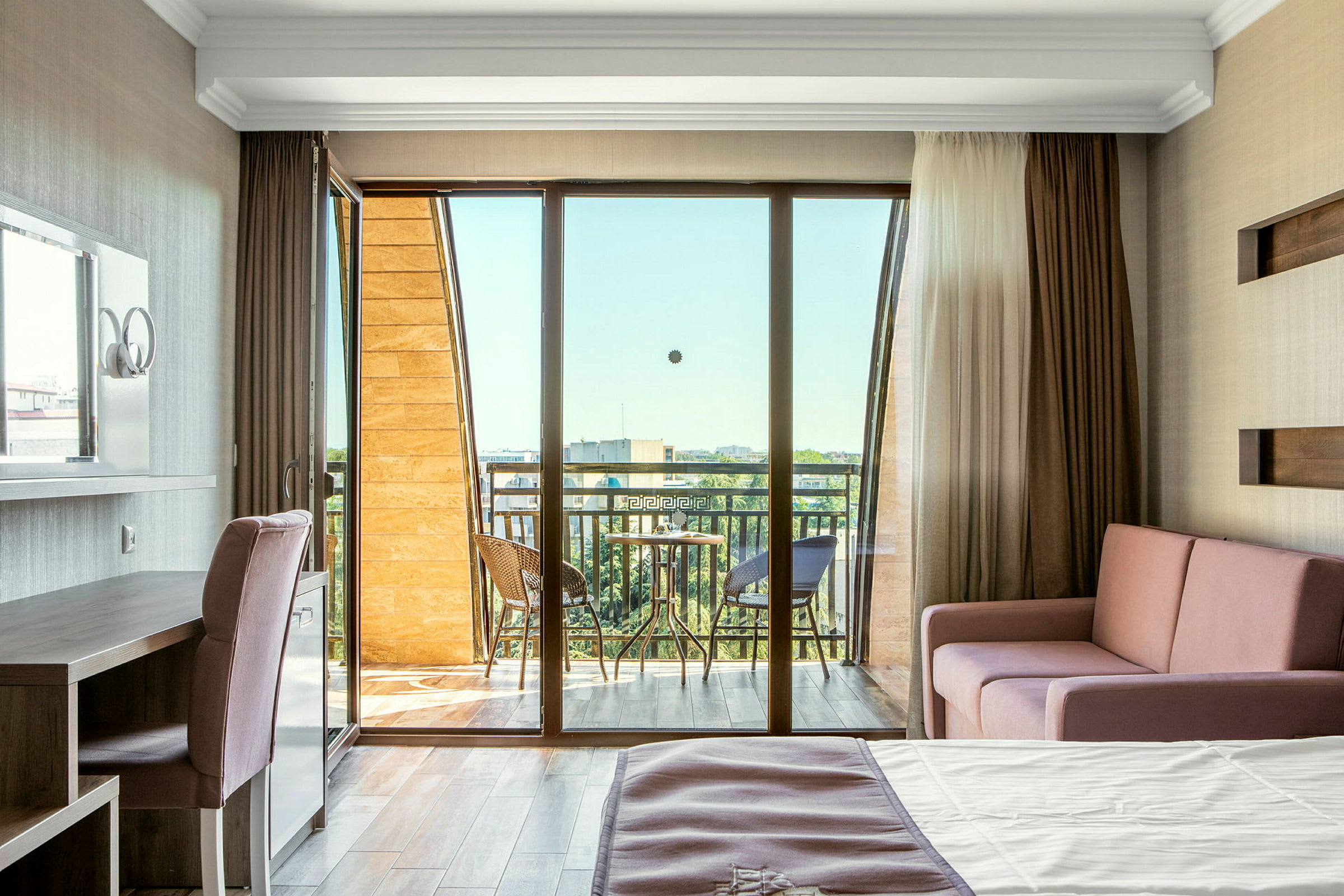 Valoisa hotellihuone parvekkeella, jossa on sänky, sohva ja kirjoituspöytä. (Tekoälyn luoma teksti)