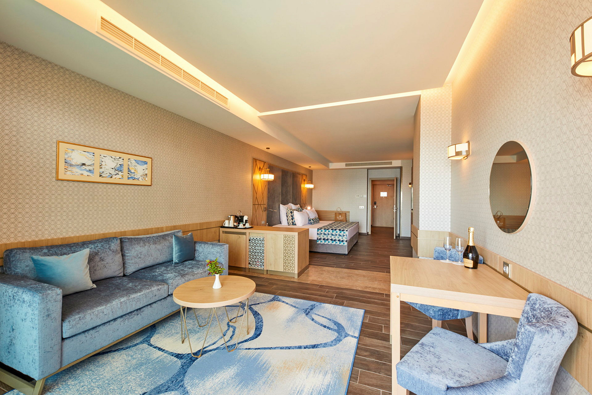 Hotellihuoneen sisustus, jossa on sohva, sohvapöytä, ruokapöytä ja sänky. (Tekoälyn luoma teksti)