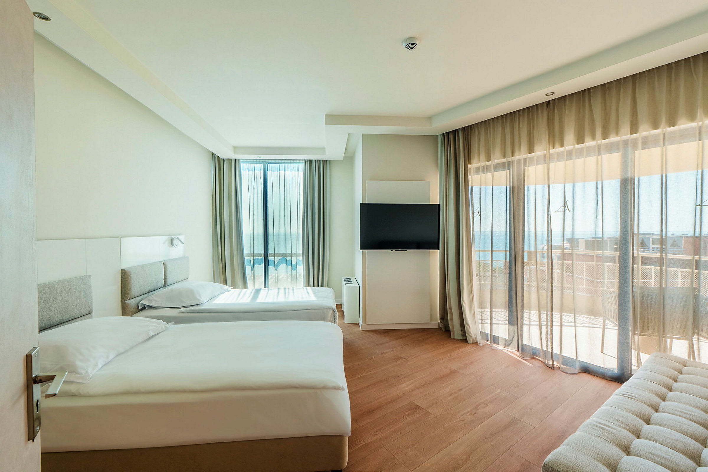 Moderni hotellihuone, jossa kaksi erillistä vuodetta, taulutelevisio ja parveke merinäköalalla. (Tekoälyn luoma teksti)