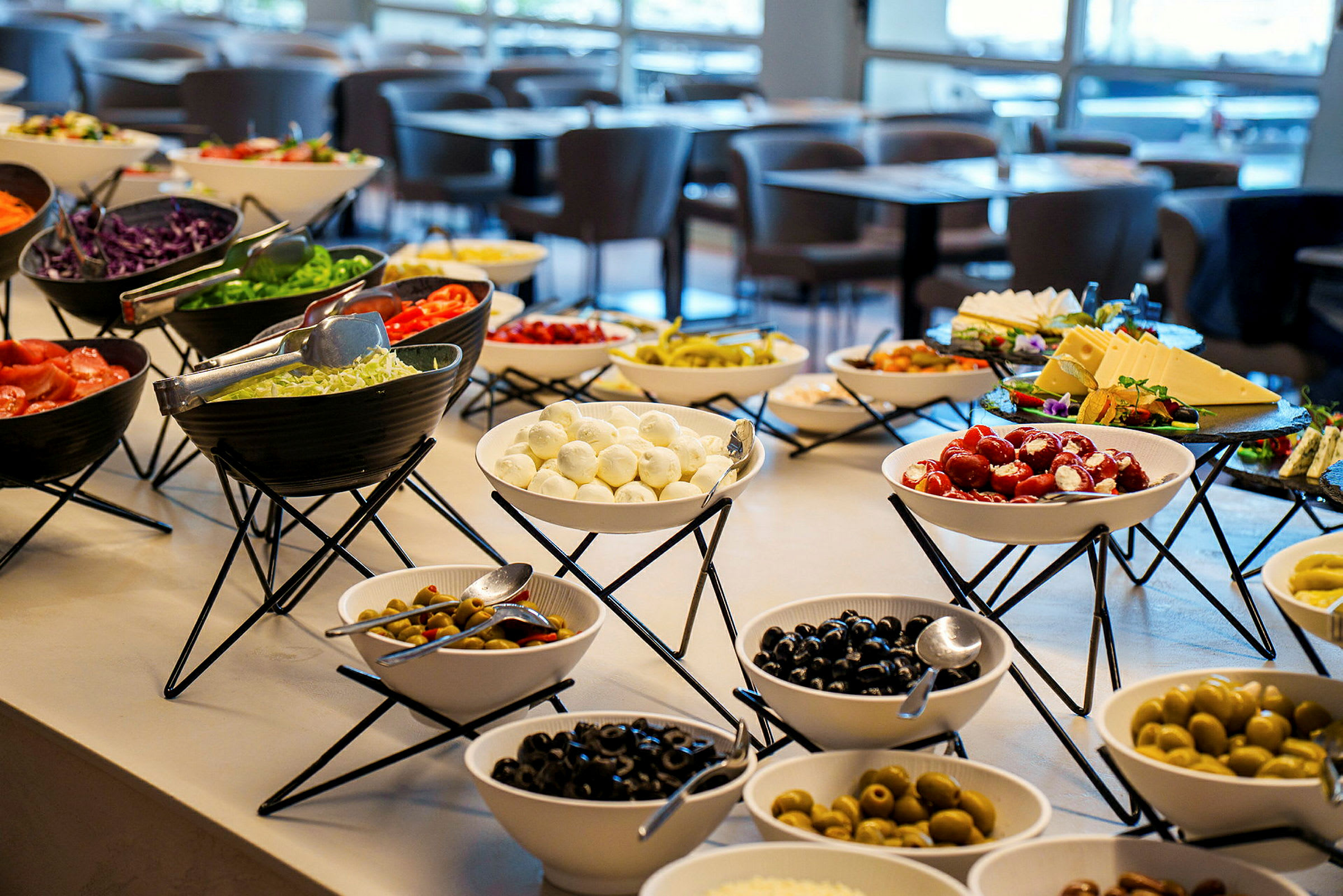 Ravintolassa buffetpöytä, jossa on erilaisia kulhoja täynnä vihanneksia, juustoja ja oliiveja. (Tekoälyn luoma teksti)