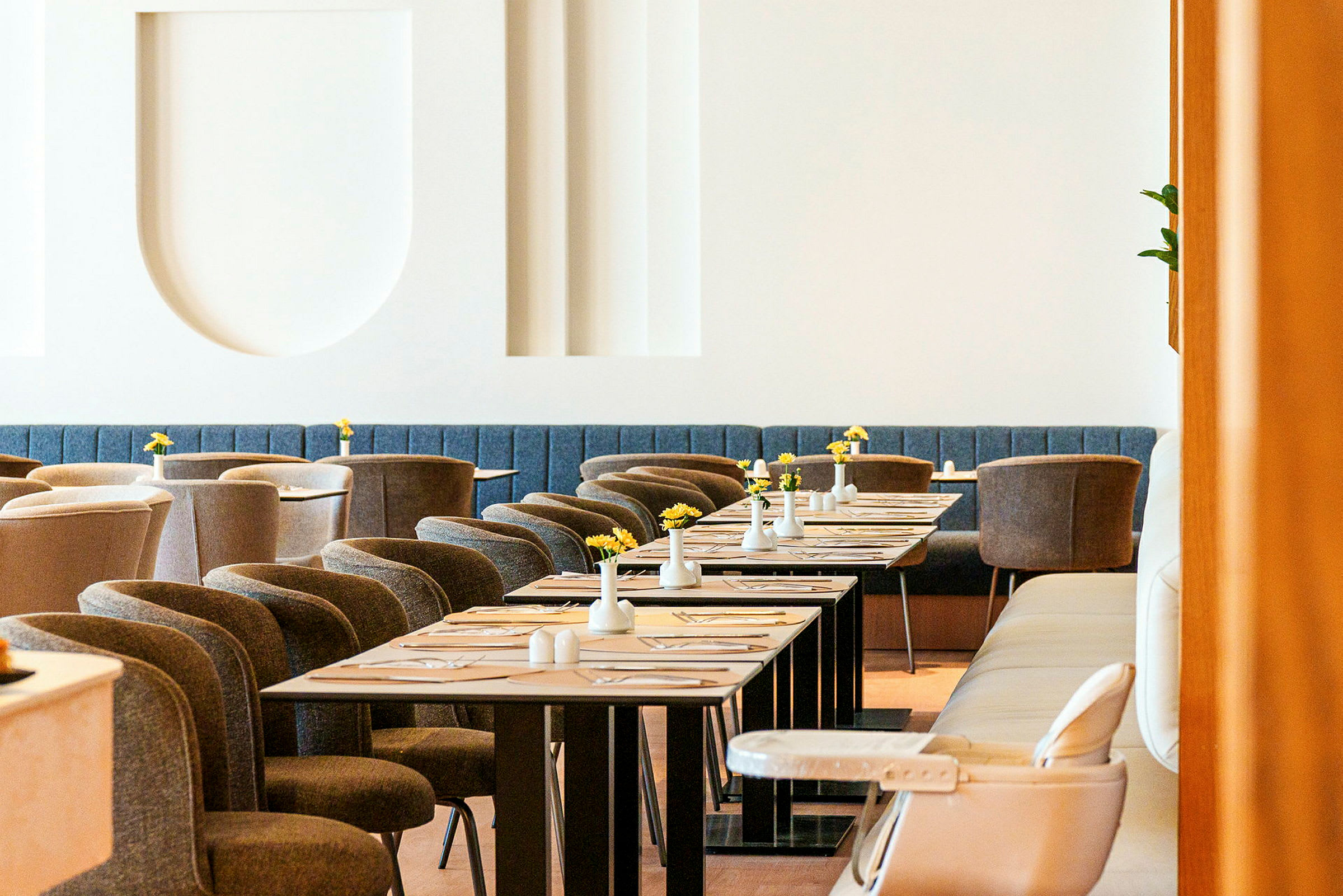 Tyylikäs ravintola, jossa on modernit huonekalut, katetut pöydät ja pieniä maljakoita keltaisilla kukilla. (Tekoälyn luoma teksti)