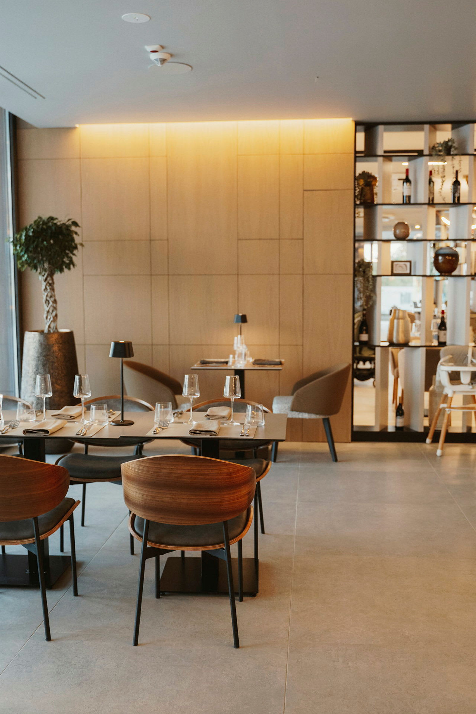 Moderni ravintola, jossa on puupaneeleja, tyylikkäät pöydät ja tuolit sekä kattaukset laseineen ja lautasineen. (Tekoälyn luoma teksti)