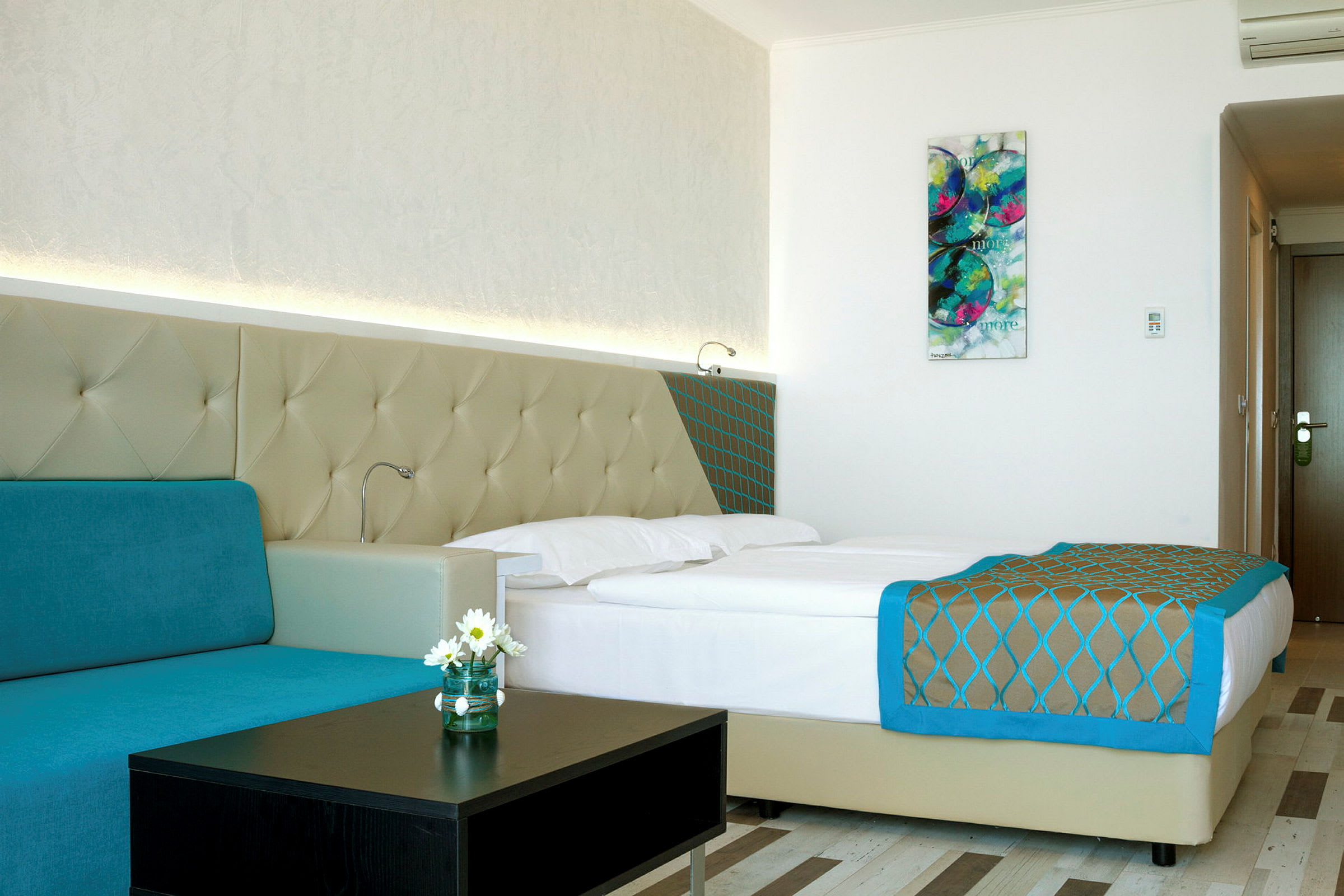 Moderni hotellihuone, jossa on parivuode, turkoosi sohva ja seinätaide. (Tekoälyn luoma teksti)