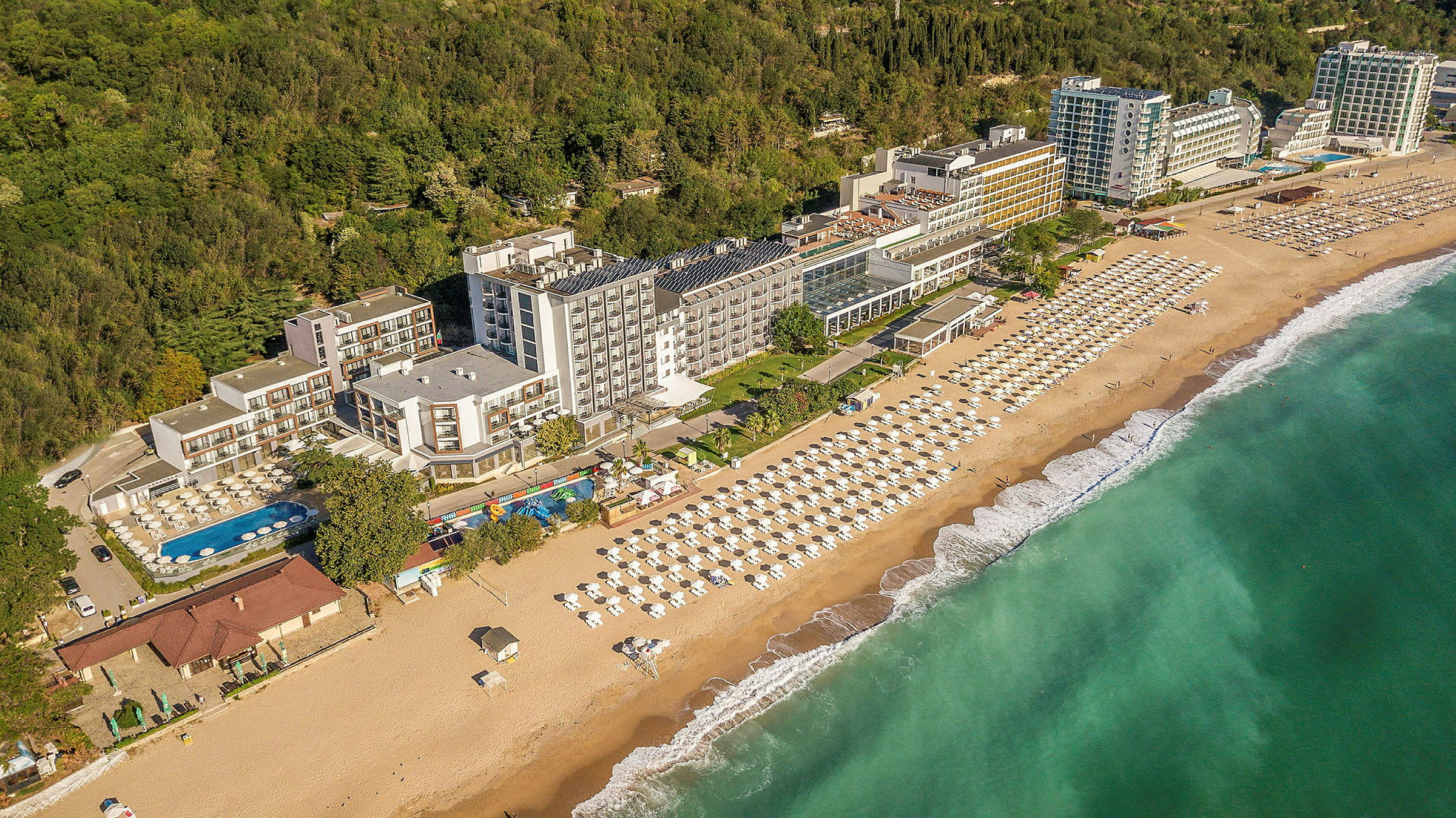 Näköala rannikon hotellista, jossa on ranta ja aurinkovarjoja sekä vehreys taustalla. (Tekoälyn luoma teksti)