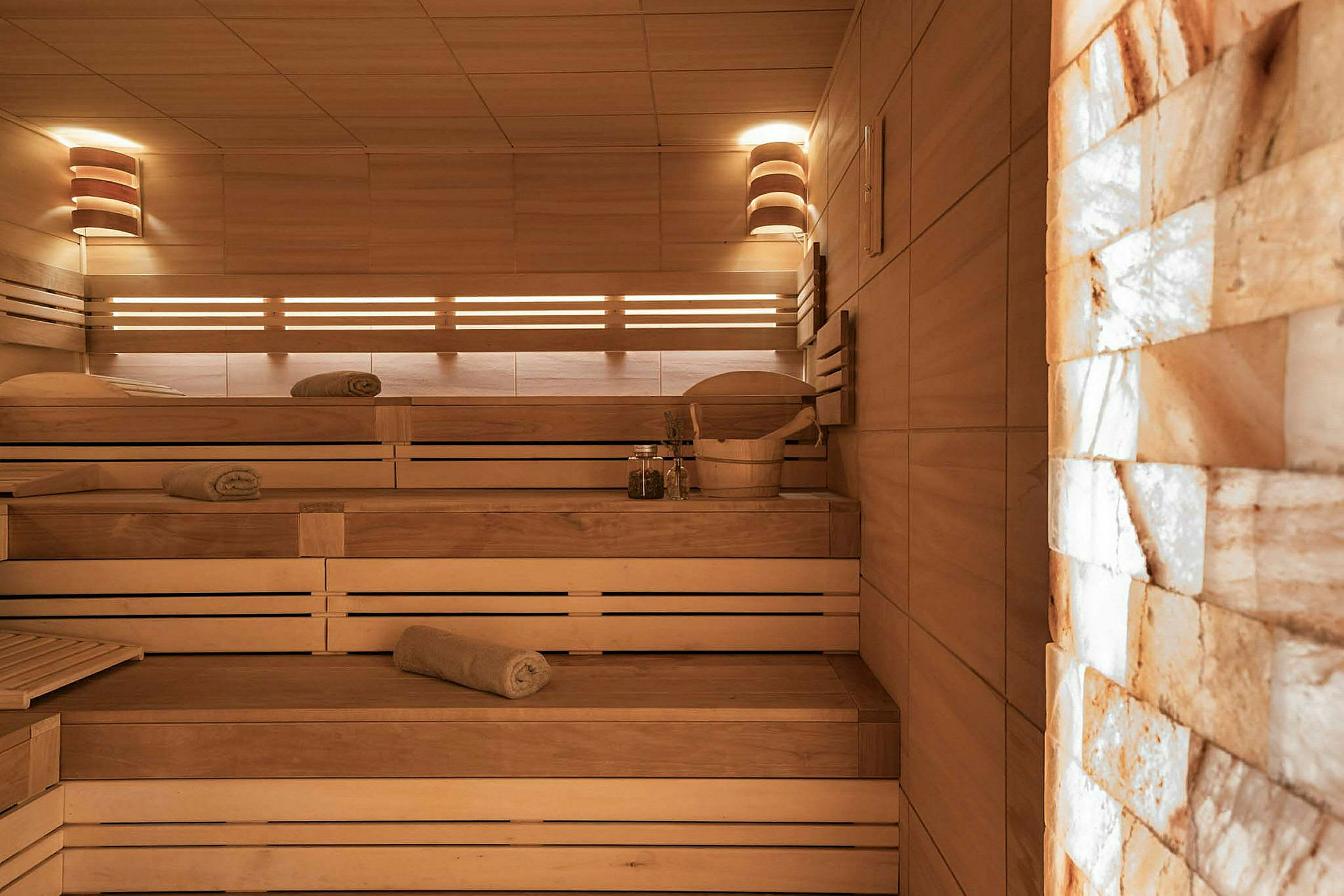 Sauna, jossa on puusisustus, useita istumatasoja ja penkeille asetettuja pyyhkeitä. (Tekoälyn luoma teksti)