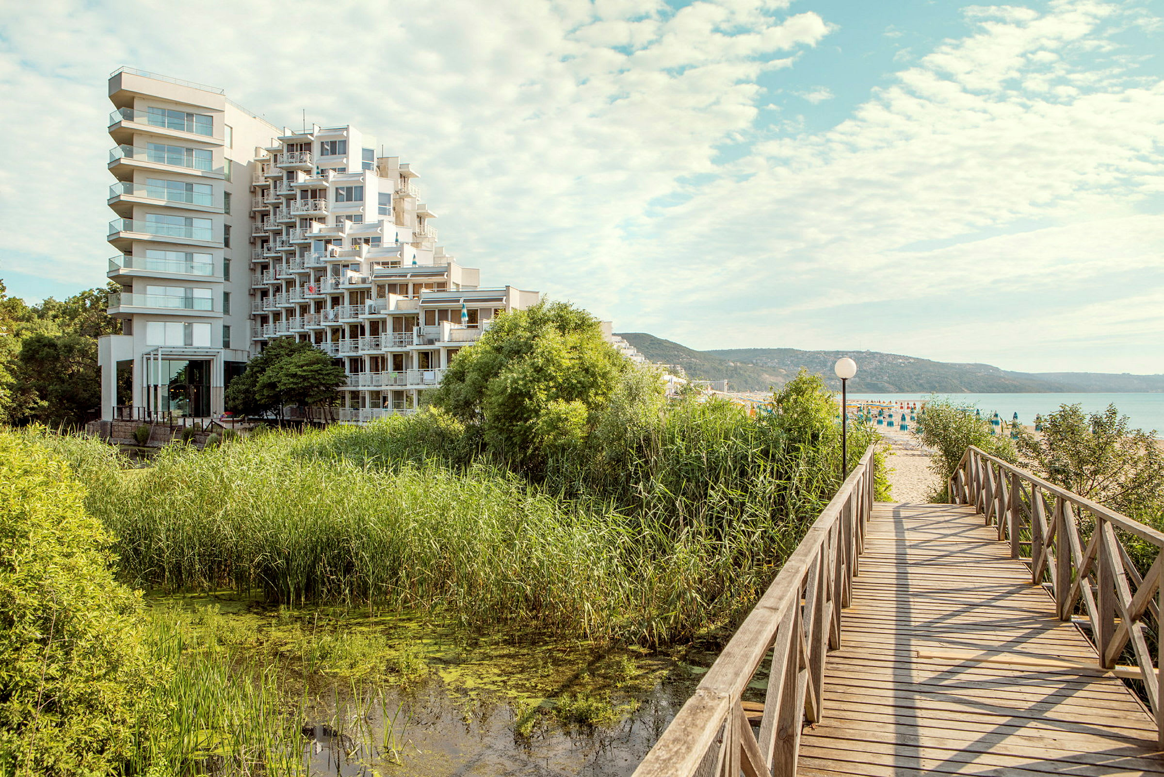Moderni hotellirakennus sijaitsee lähellä vehreää aluetta ja vesistöä, ja puusilta johtaa hiekkarannalle. (Tekoälyn luoma teksti)